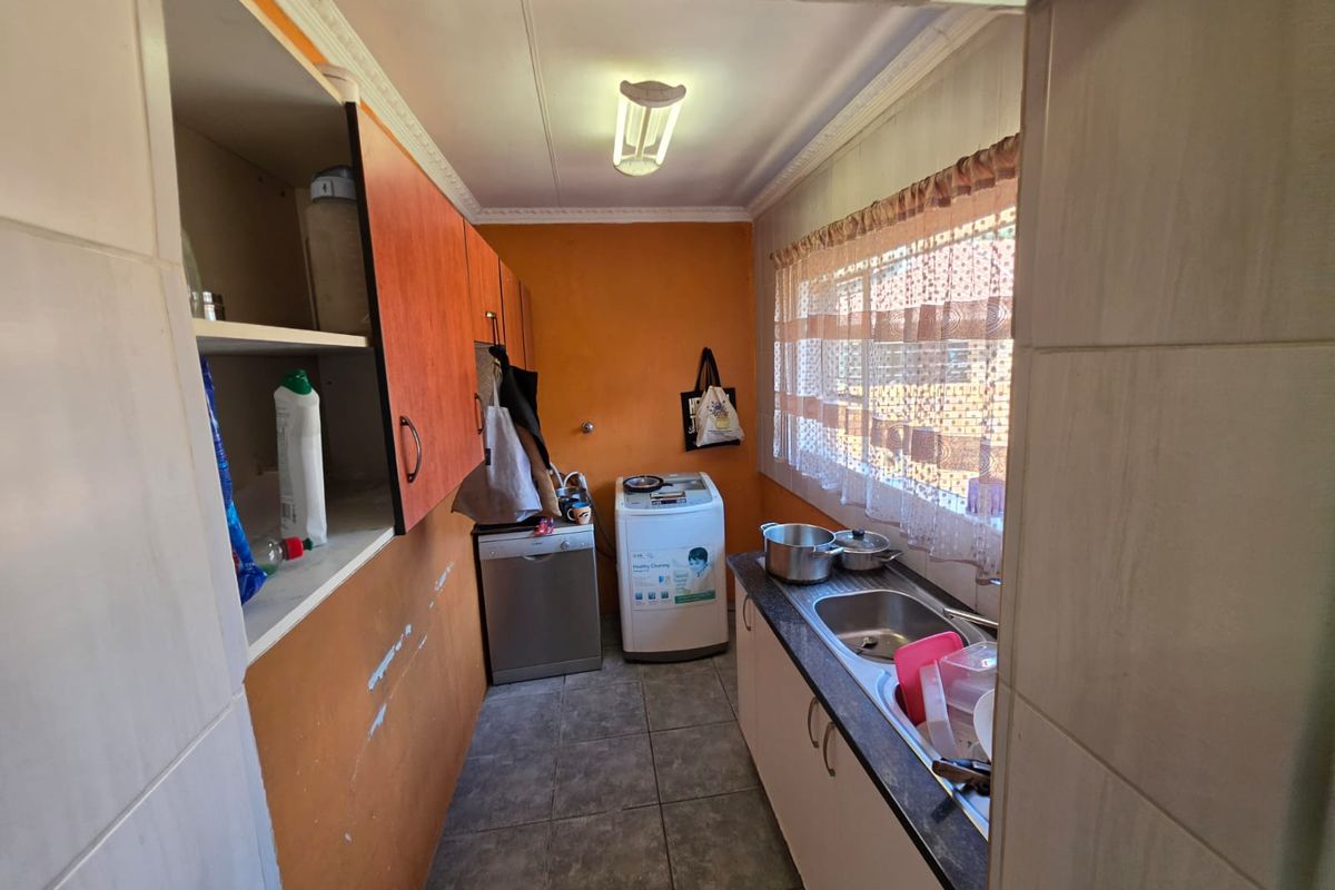 A functional laundry room featuring built-in cabinetry, a stainless steel sink, and tiled flooring, requiring some cosmetic updates to the wall finishes.