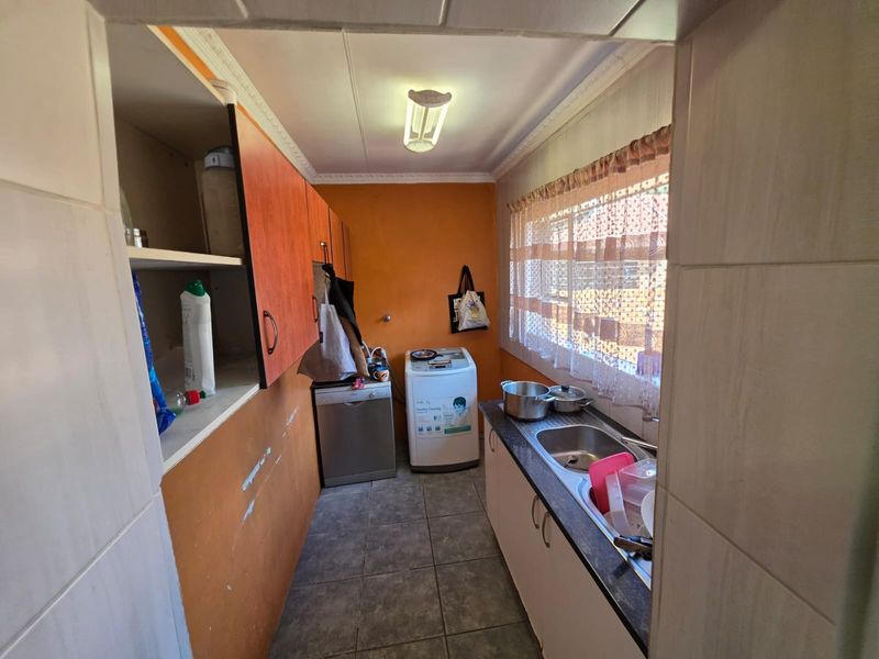 A functional laundry room featuring built-in cabinetry, a stainless steel sink, and tiled flooring, requiring some cosmetic updates to the wall finishes.
