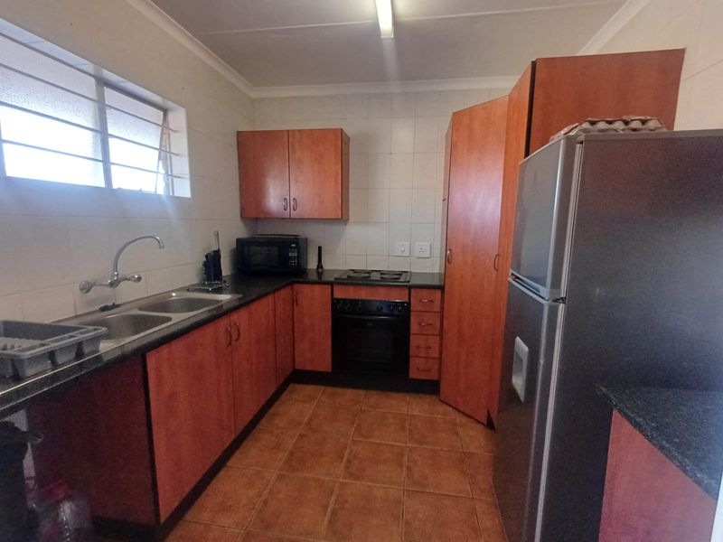 Functional kitchen featuring laminate cabinetry, double bowl sink, built-in oven, electric hob, and tiled splashbacks with neutral floor tiles.