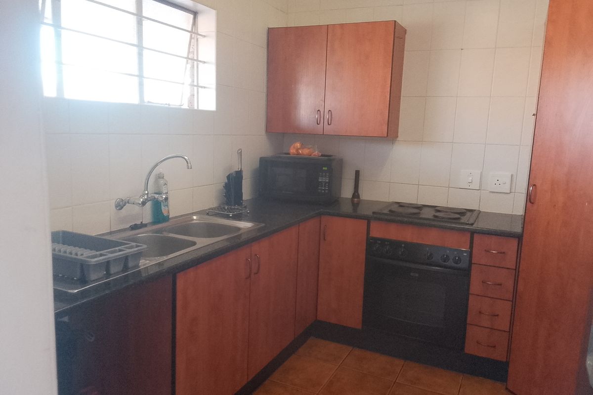 A functional kitchen featuring laminate cabinetry, a double bowl sink, built-in oven, and electric hob with tiled splashbacks and flooring.