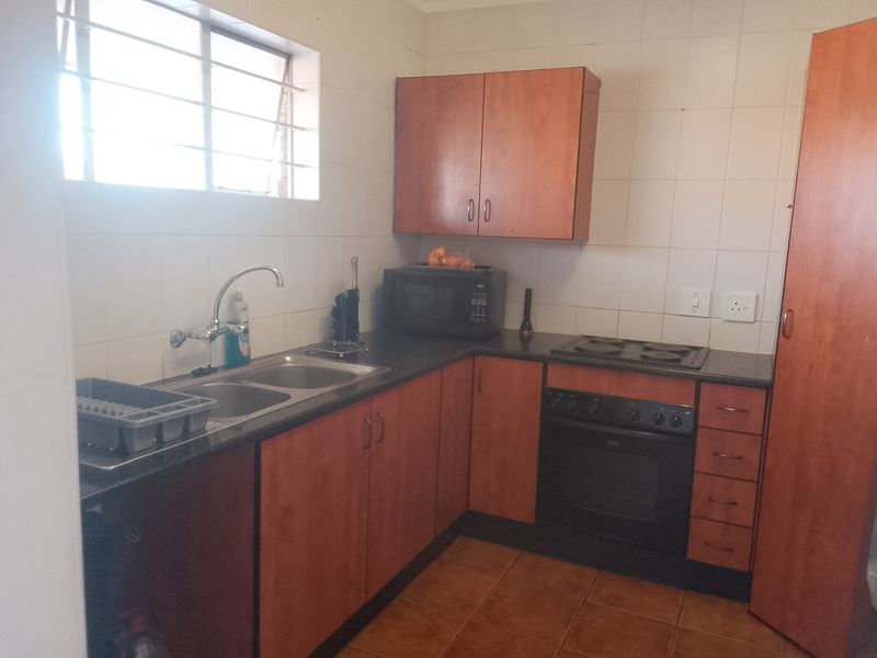 A functional kitchen featuring laminate cabinetry, a double bowl sink, built-in oven, and electric hob with tiled splashbacks and flooring.