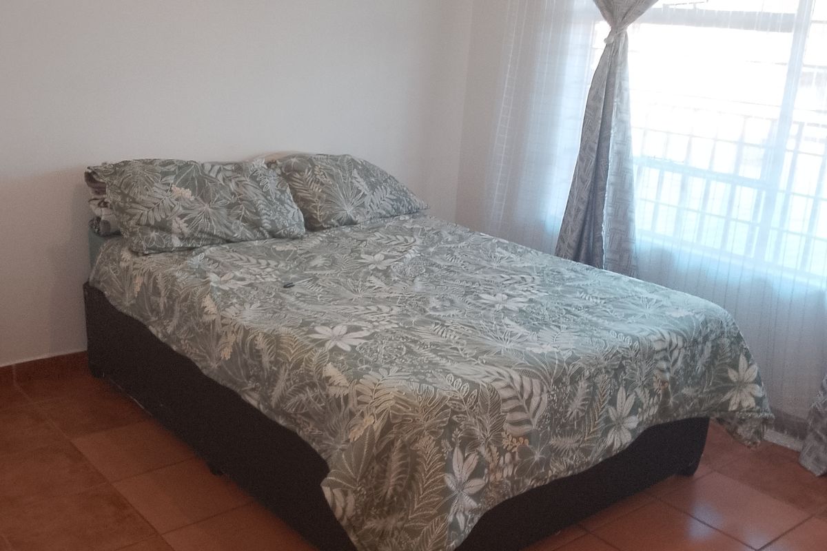 A simple bedroom featuring tiled flooring and a window fitted with security bars, providing natural light.