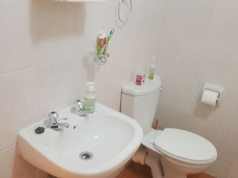 A functional bathroom featuring a pedestal sink, standard toilet, and wall-mounted medicine cabinet with neutral wall tiling and terracotta-style floor tiles.