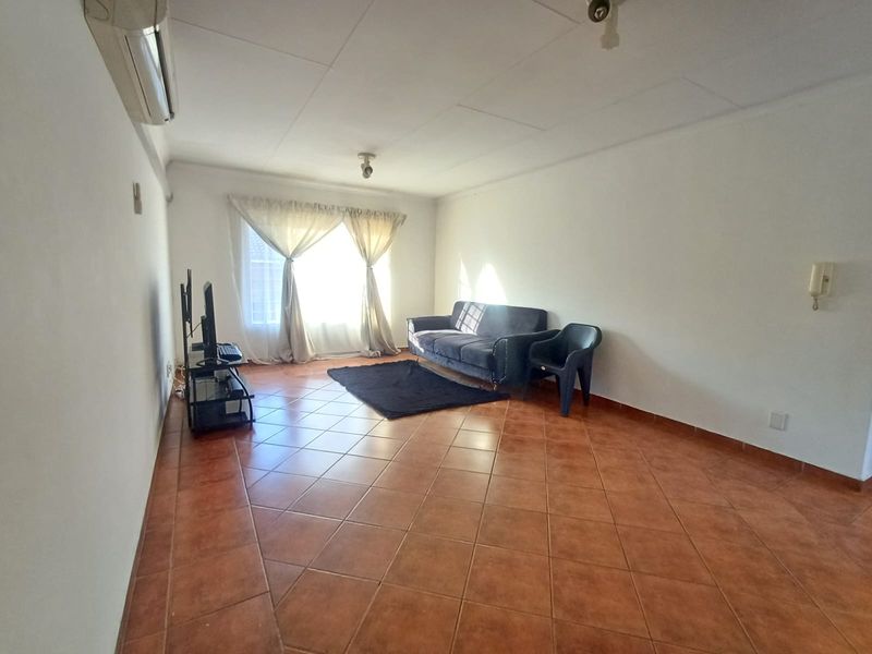 A spacious living room featuring terracotta-style floor tiles, an installed air conditioning unit, and an intercom system, offering a functional and neutral living space.