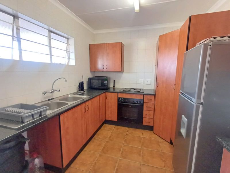 A functional kitchen featuring laminate cabinetry, a double bowl sink, built-in oven, electric hob, and tiled flooring with a practical layout.