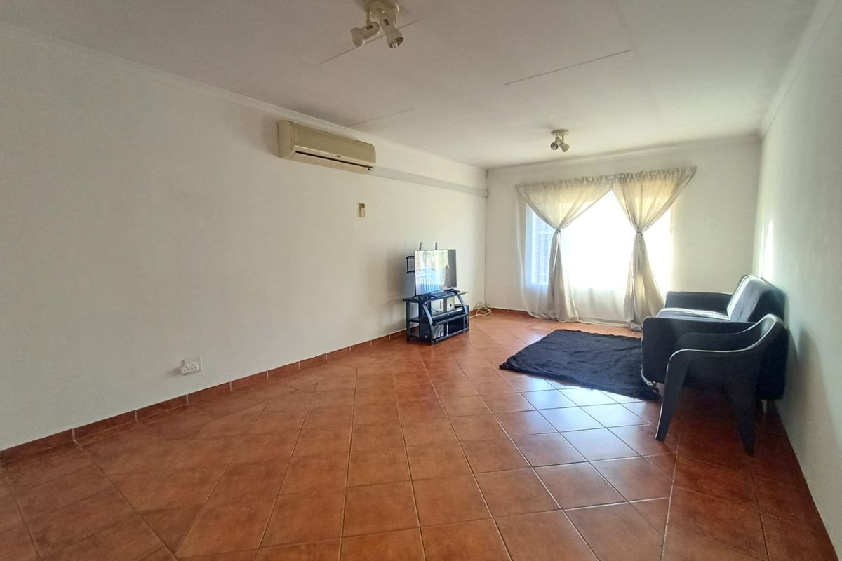 A living room featuring ceramic tile flooring, a wall-mounted air conditioning unit, and natural light from a window with curtains.