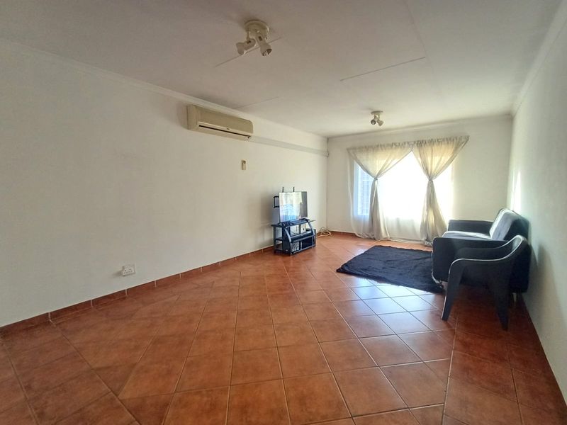A living room featuring ceramic tile flooring, a wall-mounted air conditioning unit, and natural light from a window with curtains.