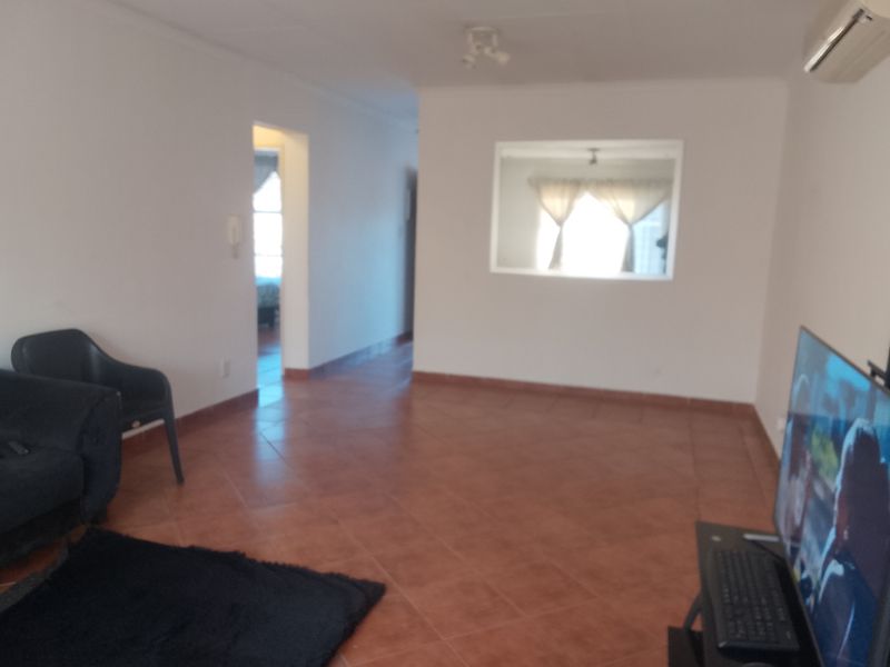 A living room featuring tiled flooring, a wall-mounted air conditioning unit, and an interior window cutout looking into an adjacent space.