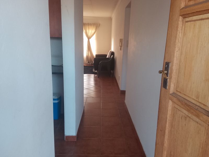 A view from the entrance looking down a tiled hallway towards the living area, featuring a wooden door and wall-mounted intercom system.