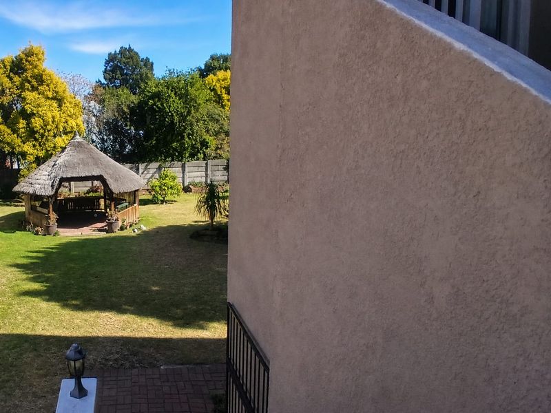 A view of the rear garden featuring a thatched gazebo, paved patio area, and a secure boundary wall.