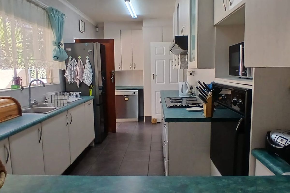 Functional kitchen featuring white cabinetry, laminate countertops, built-in oven, hob, and extractor fan with tiled flooring and natural light.