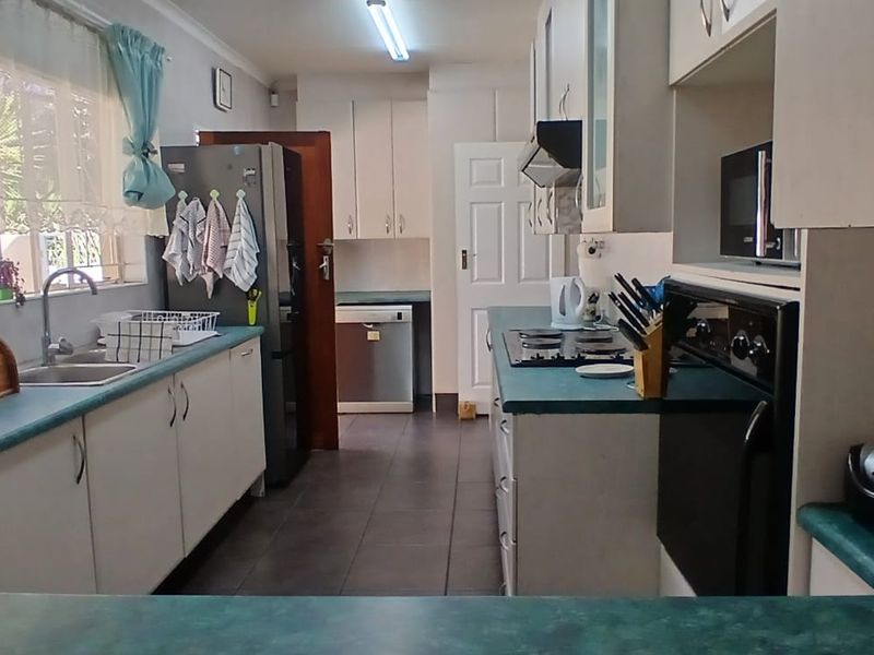 Functional kitchen featuring white cabinetry, laminate countertops, built-in oven, hob, and extractor fan with tiled flooring and natural light.
