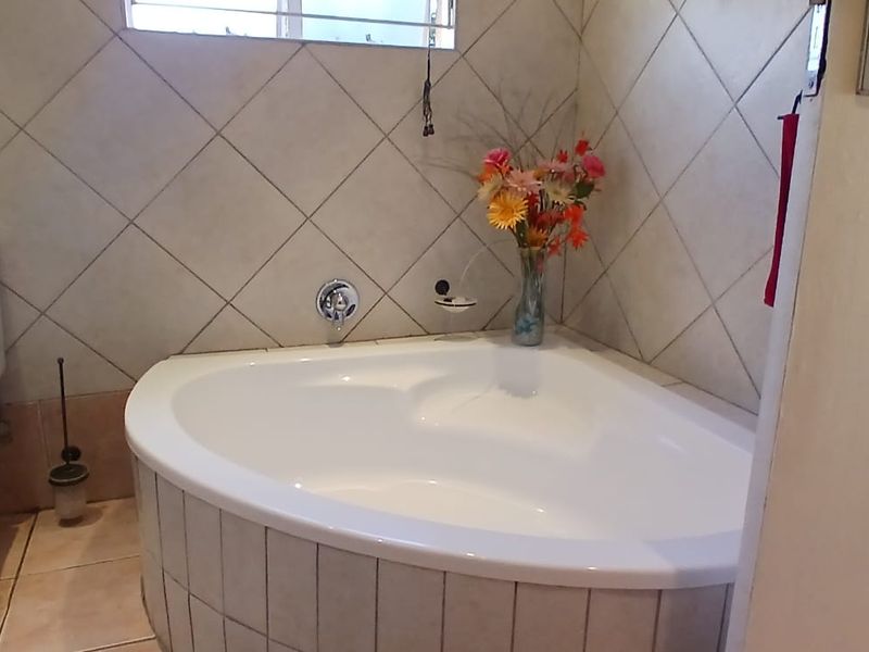 A functional bathroom featuring a corner bathtub, tiled walls, and a standard toilet, offering a clean and practical layout.