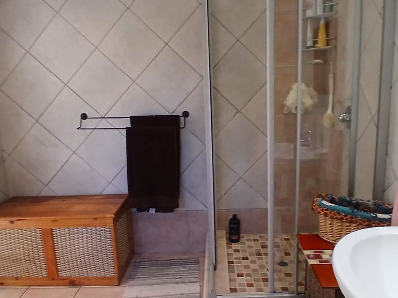 A functional bathroom featuring a shower enclosure with tiled walls, a pedestal basin with chrome mixer tap, and neutral floor tiling.