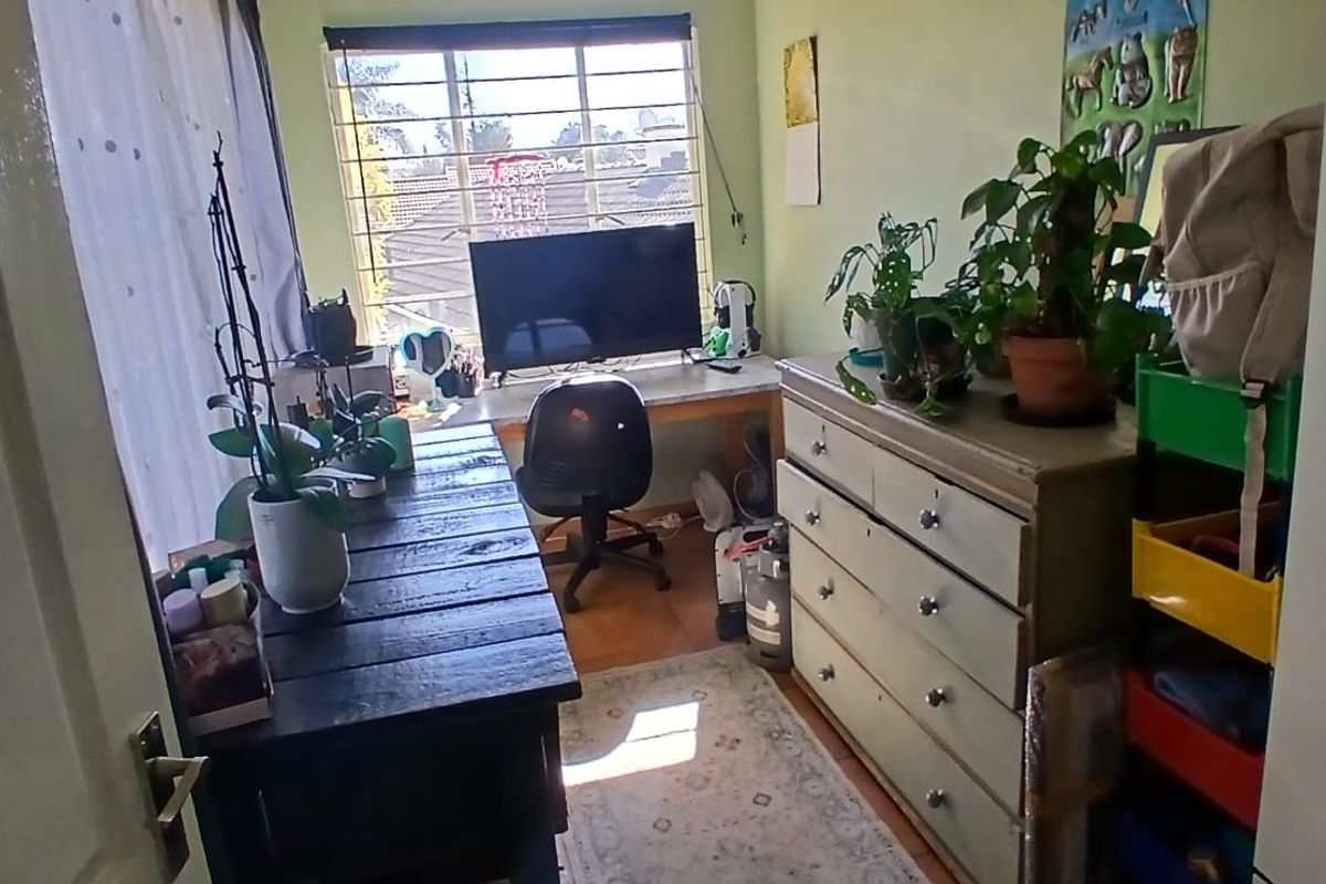 A compact bedroom featuring laminate flooring, a built-in desk area, and security bars on the window.