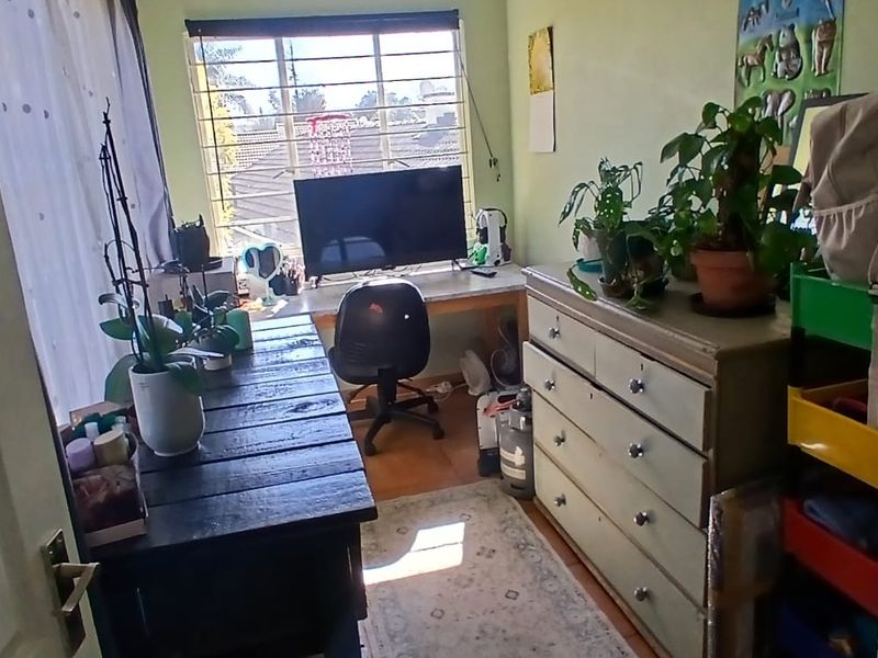 A compact bedroom featuring laminate flooring, a built-in desk area, and security bars on the window.