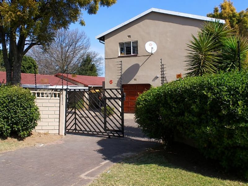Front exterior view of the property featuring a paved driveway, secure metal gate, boundary wall with electric fencing, and a garage entrance.