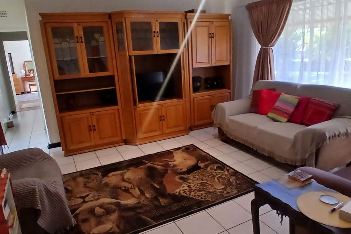 A living room featuring tiled flooring and large windows with curtain rails, providing a functional and well-lit space.
