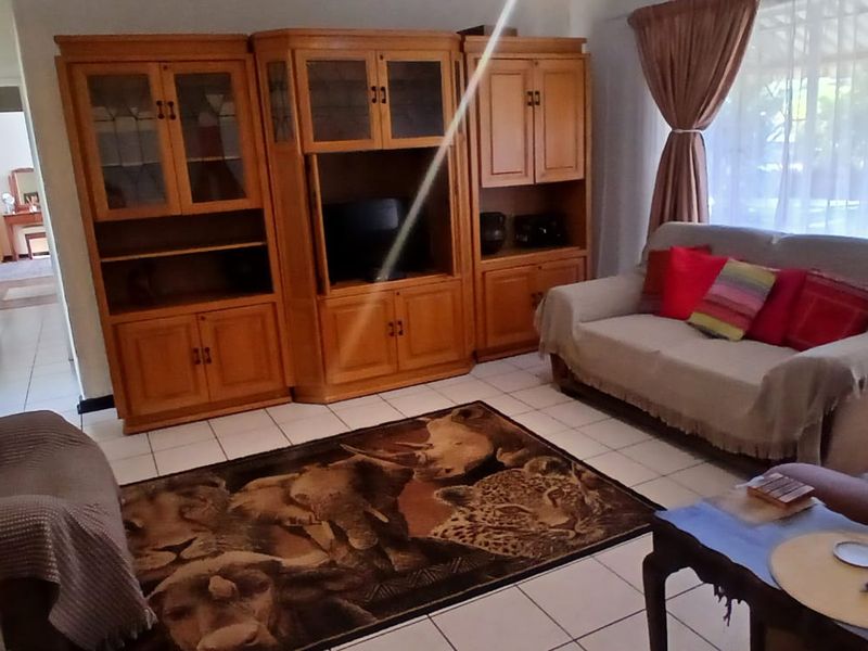 A living room featuring tiled flooring and large windows with curtain rails, providing a functional and well-lit space.