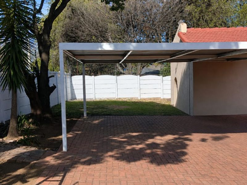 A functional outdoor carport area featuring a paved driveway, secure perimeter walling with electric fencing, and direct access to the main house structure.