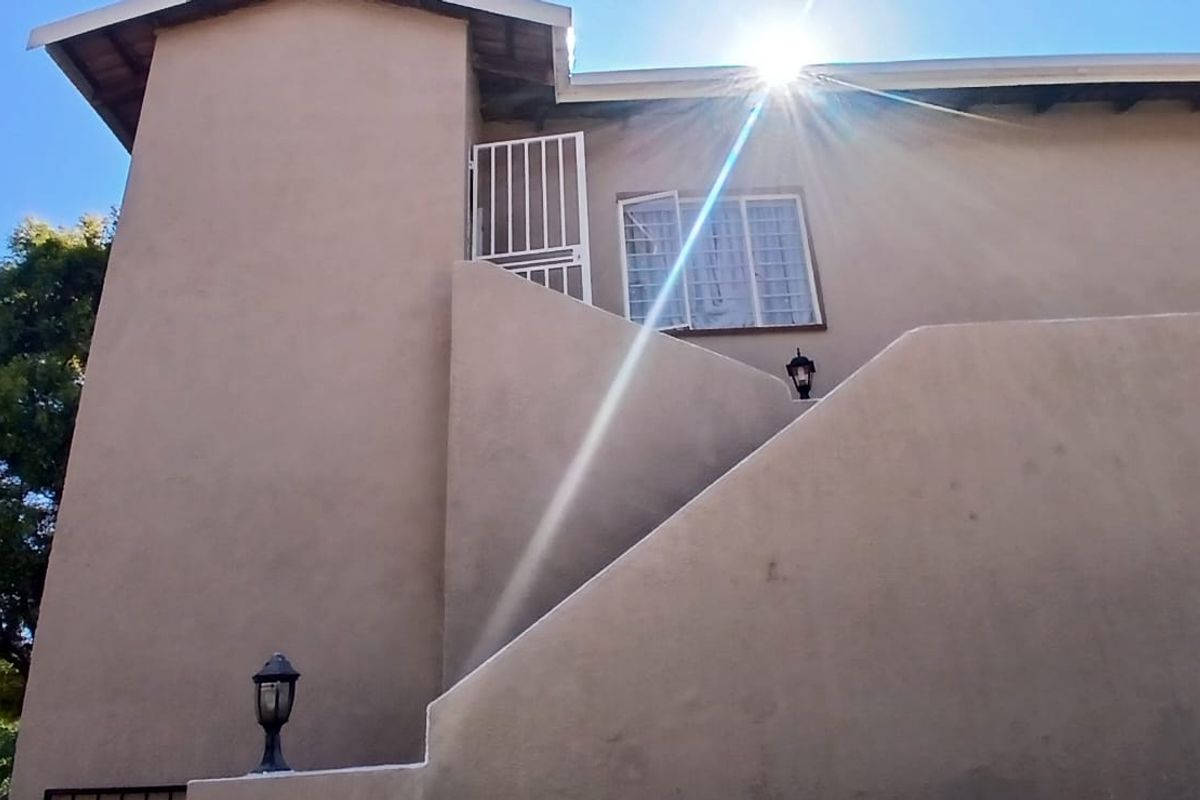 Rear exterior view of the property featuring an external staircase, security gate, and wall-mounted lighting fixtures.