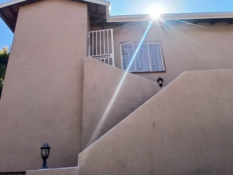 Rear exterior view of the property featuring an external staircase, security gate, and wall-mounted lighting fixtures.