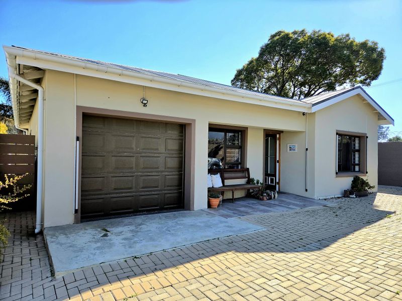 Front elevation of a single-story house featuring a garage, paved driveway, and a covered entrance area with aluminium window frames.