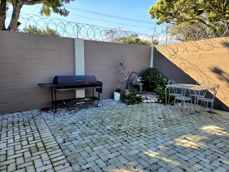 A paved outdoor patio area enclosed by a high perimeter wall with security razor wire, featuring a dedicated space for outdoor cooking.