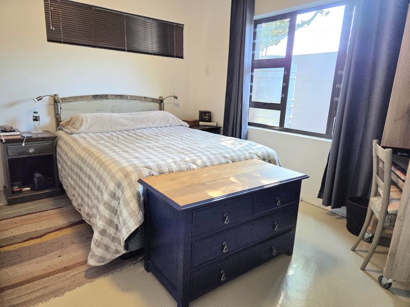 A functional bedroom featuring neutral walls, polished concrete flooring, and natural light provided by two windows.