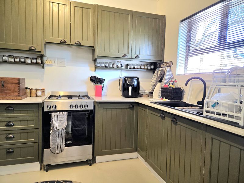 A functional kitchen featuring olive green cabinetry, a stainless steel gas stove with oven, and a dark sink with a modern faucet.