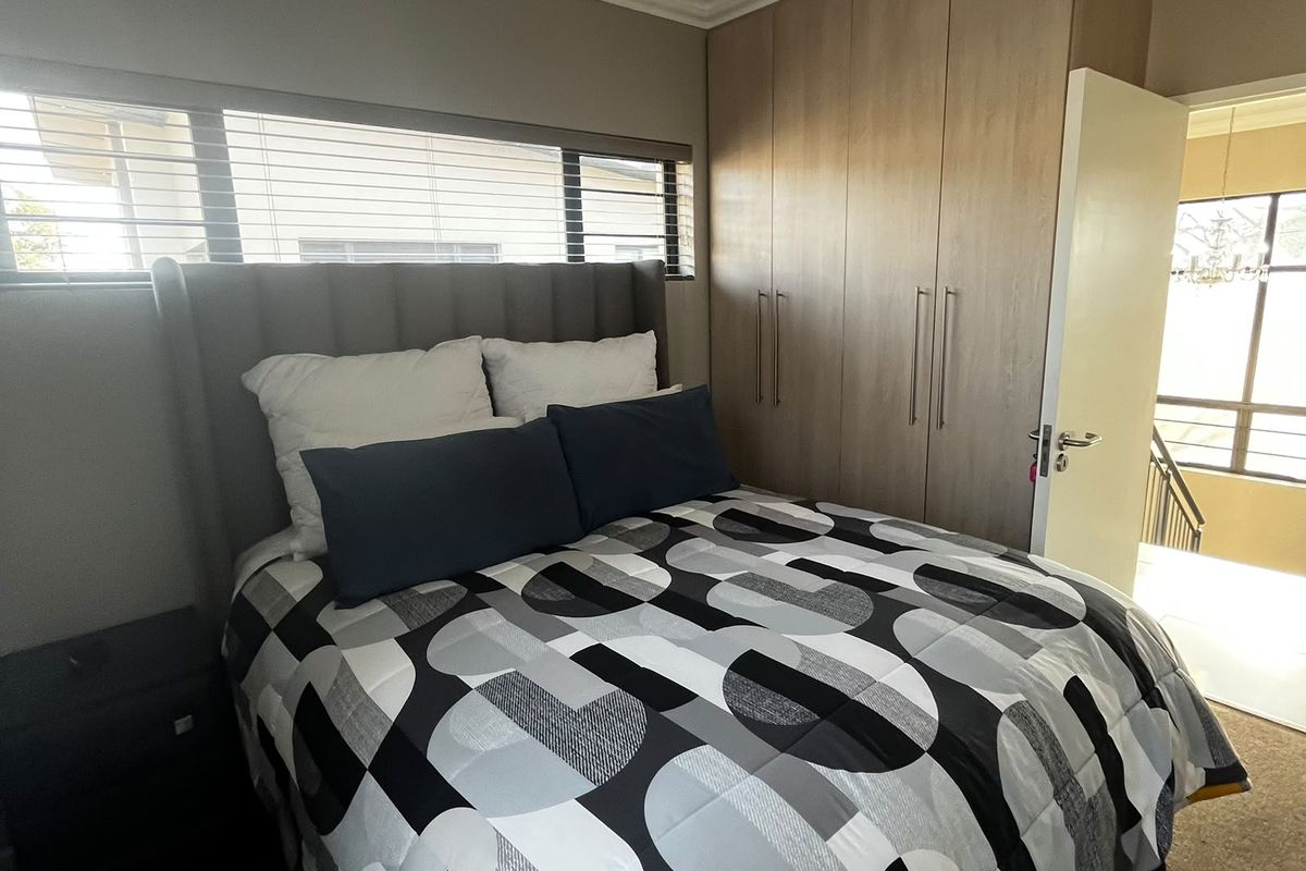 A well-lit bedroom featuring built-in wooden cupboards, recessed ceiling lighting, and horizontal window blinds, offering a functional and comfortable living space.