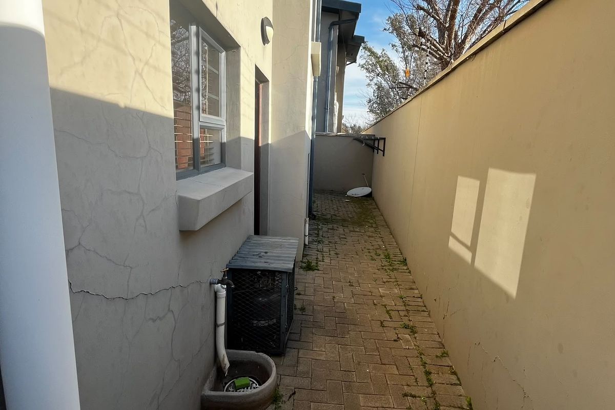 A narrow rear exterior walkway featuring paved flooring, a boundary wall, and an external water tap with a small basin.