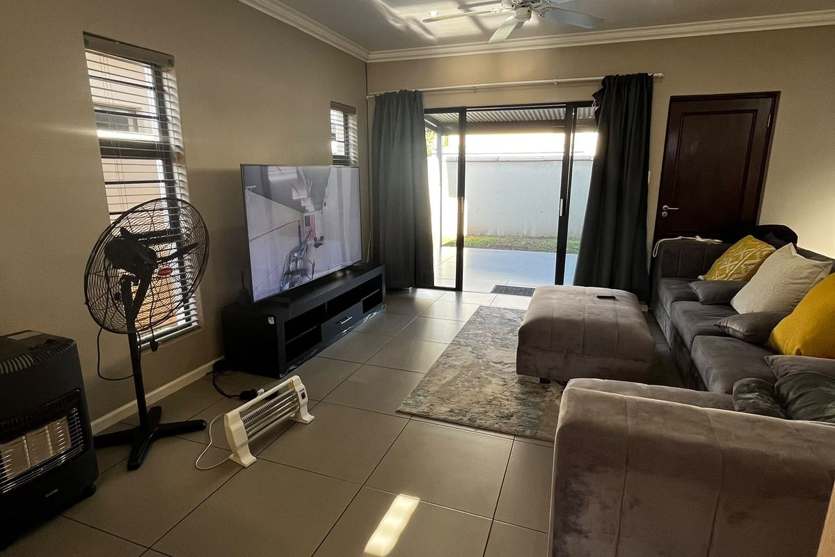A well-maintained living room featuring large floor tiles, recessed ceiling lighting, a ceiling fan, and direct access to an outdoor patio area.