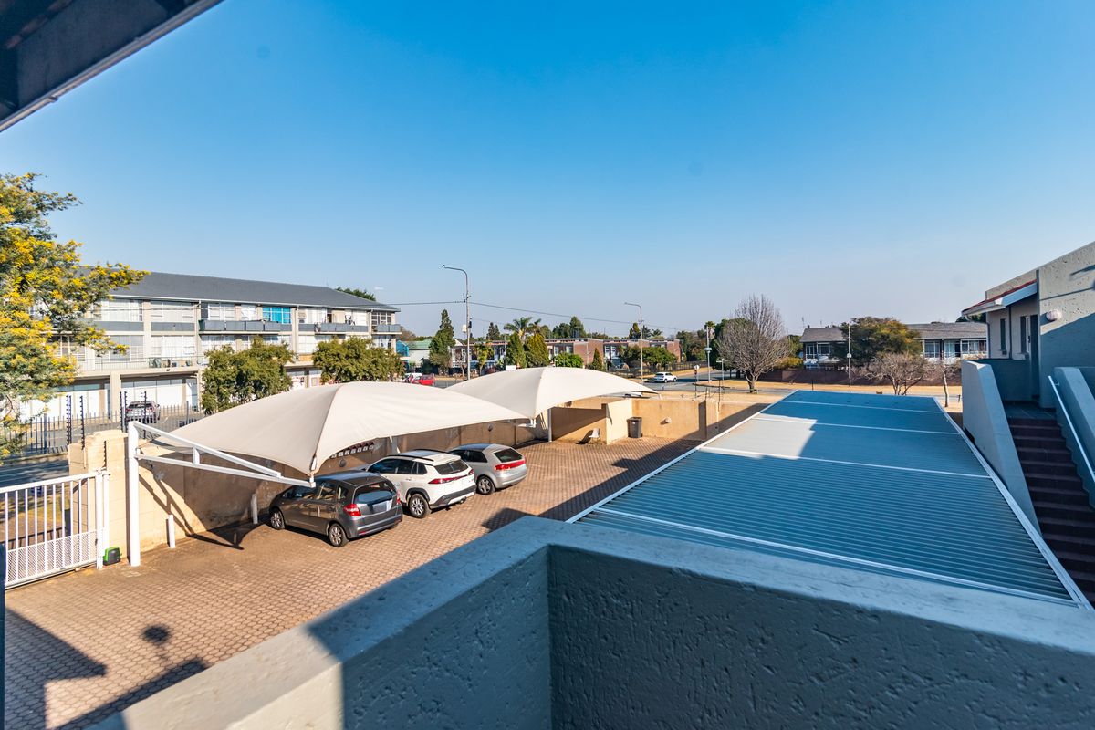 An elevated view of the apartment complex parking area featuring paved driveways, shade cloth carports, and surrounding perimeter walls.