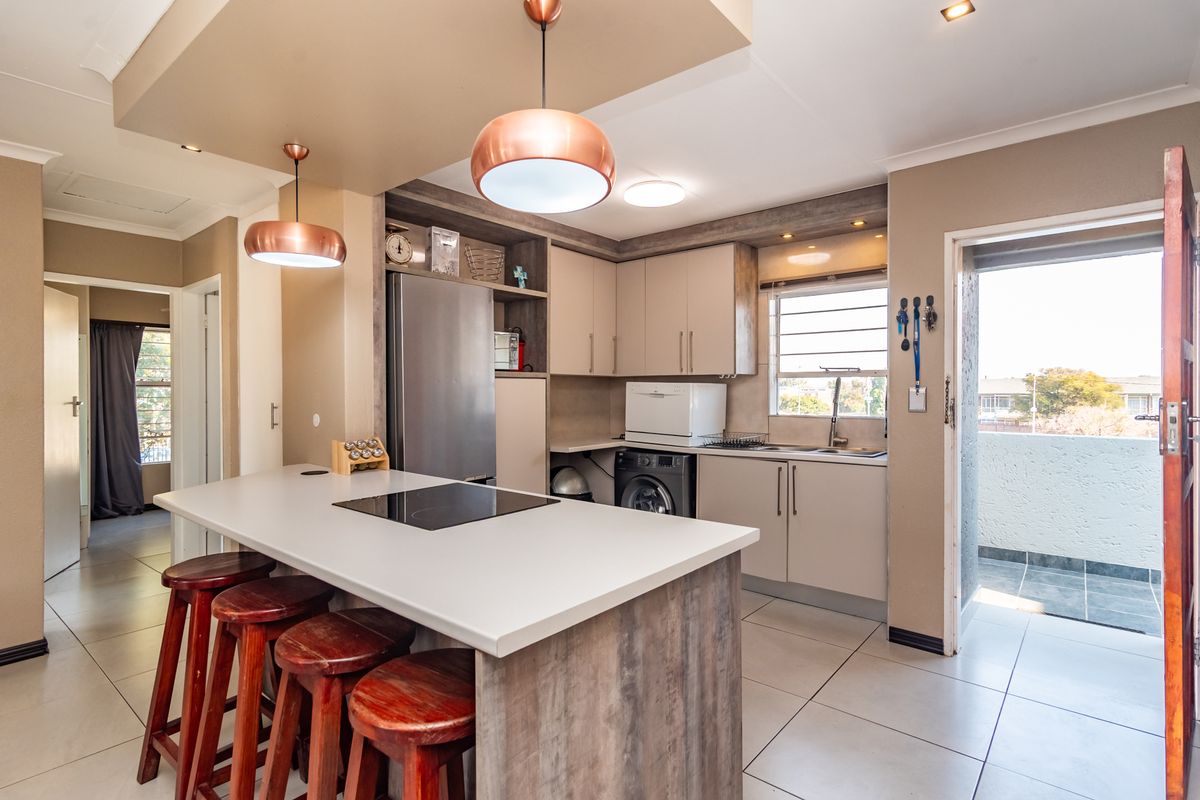 Modern kitchen featuring a central island with an integrated induction hob, ample built-in cabinetry, tiled flooring, and direct access to a balcony.