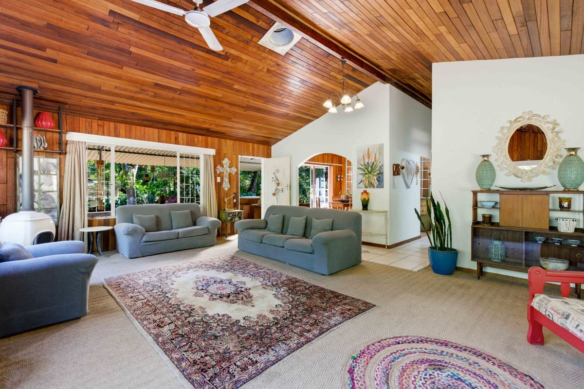 Spacious living room featuring a high timber-clad vaulted ceiling, a freestanding fireplace, and large windows providing natural light and garden views.