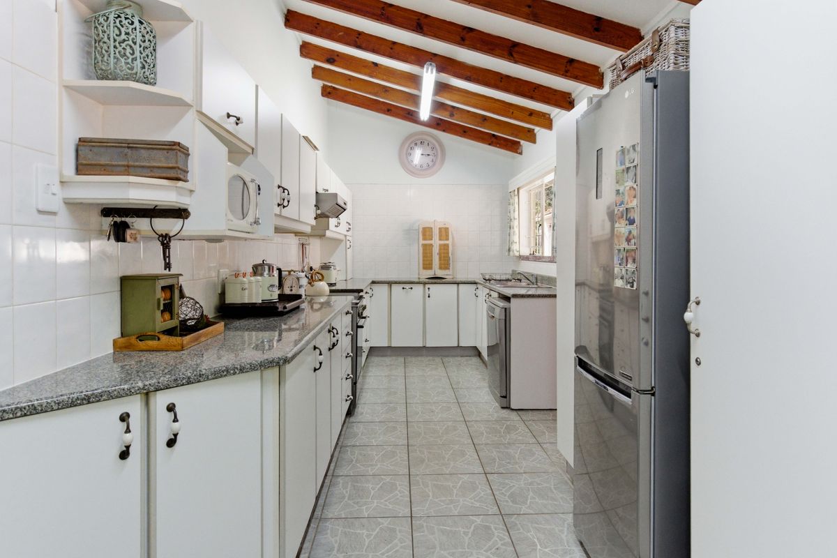 A functional galley-style kitchen featuring granite countertops, white cabinetry, tiled backsplash, and exposed timber ceiling beams, offering a classic aesthetic with practical layout.