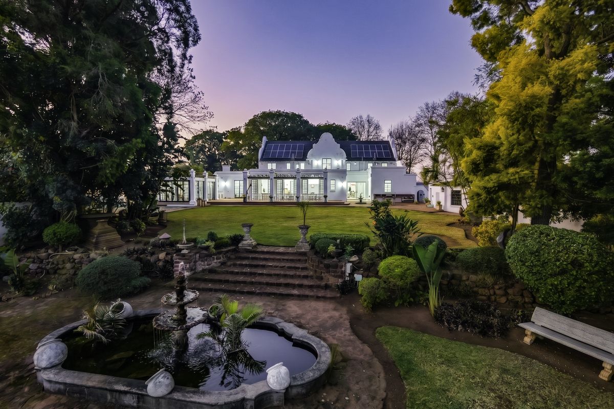 A beautifully landscaped rear garden featuring a stone fountain, tiered stone staircase, and a spacious patio overlooking the main residence.