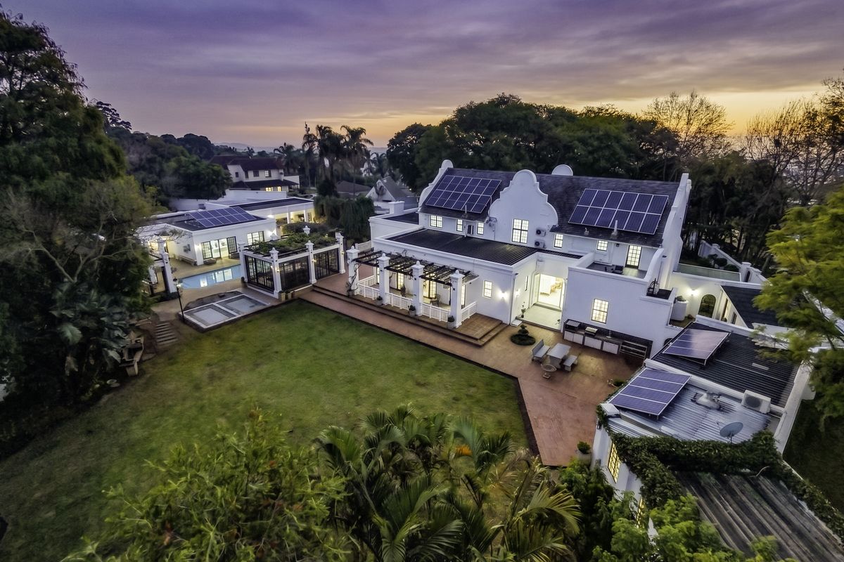Aerial view of a large residential property featuring a gabled roof, extensive solar panel installation, swimming pool, and landscaped garden with outdoor entertainment areas.