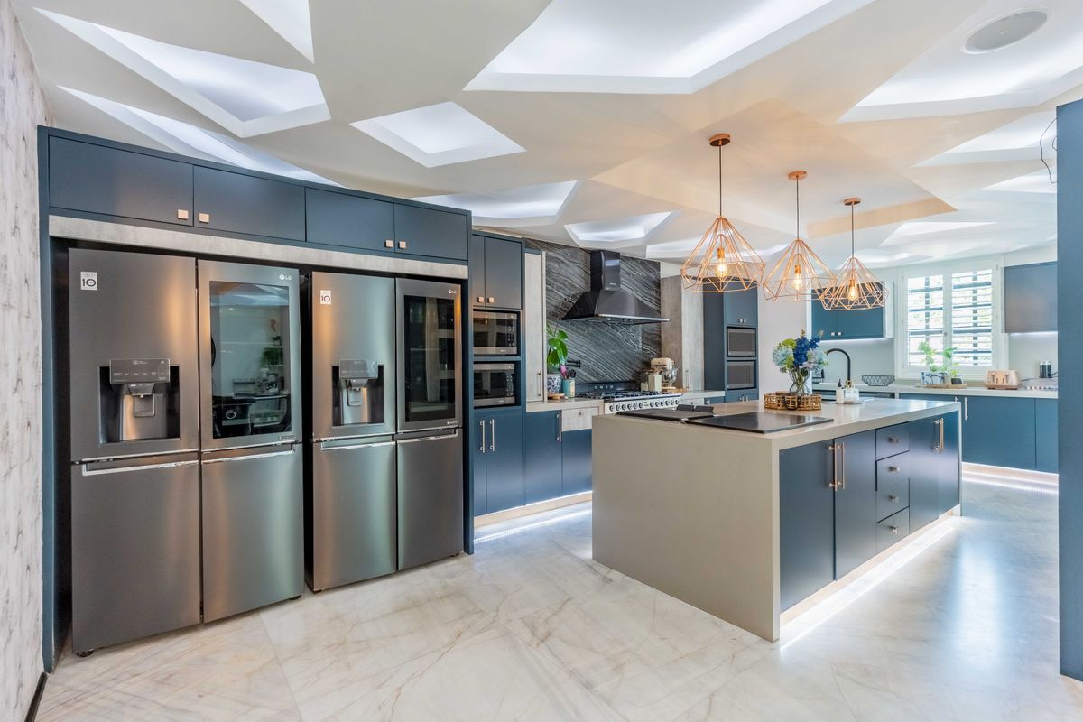 Modern, high-end kitchen featuring dark blue cabinetry, a large central island with stone countertops, integrated appliances, and a unique geometric coffered ceiling design.