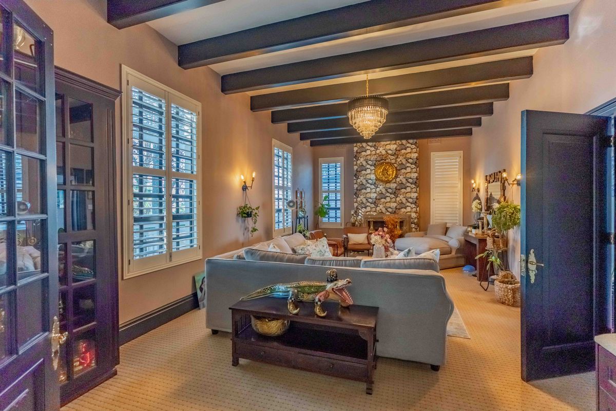 Spacious living room featuring exposed timber ceiling beams, a prominent stone fireplace, and plantation shutters, creating a warm and inviting atmosphere.