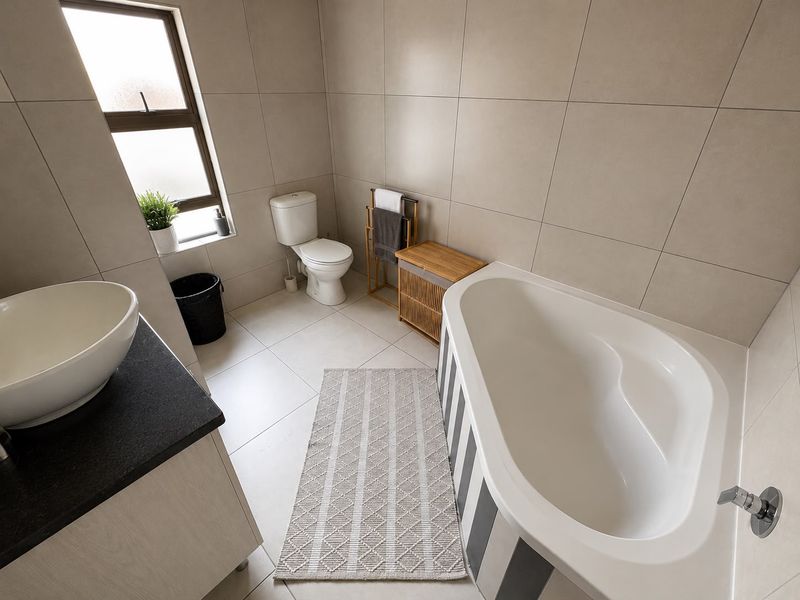 Modern bathroom featuring large-format neutral wall and floor tiles, a vessel sink vanity, and a built-in bathtub with a contemporary finish.