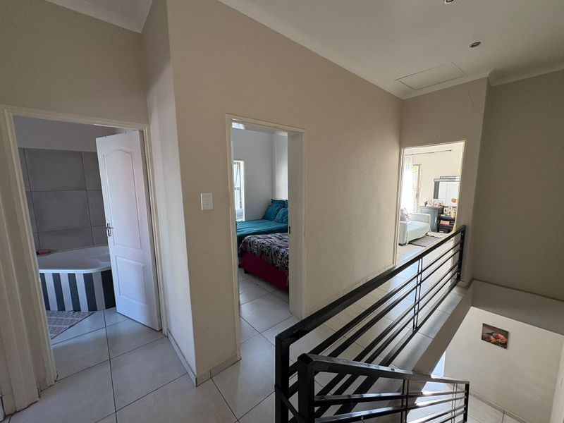Upper level hallway featuring tiled flooring, a metal balustrade overlooking the staircase, and access to multiple bedrooms and a bathroom.