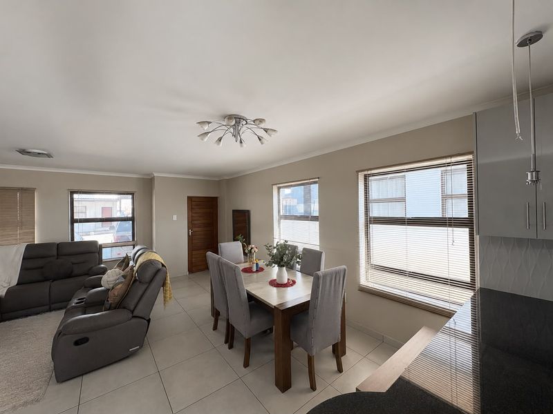 Spacious open-plan living and dining area featuring neutral tiled flooring, modern lighting, and large windows with venetian blinds, seamlessly connected to the kitchen.