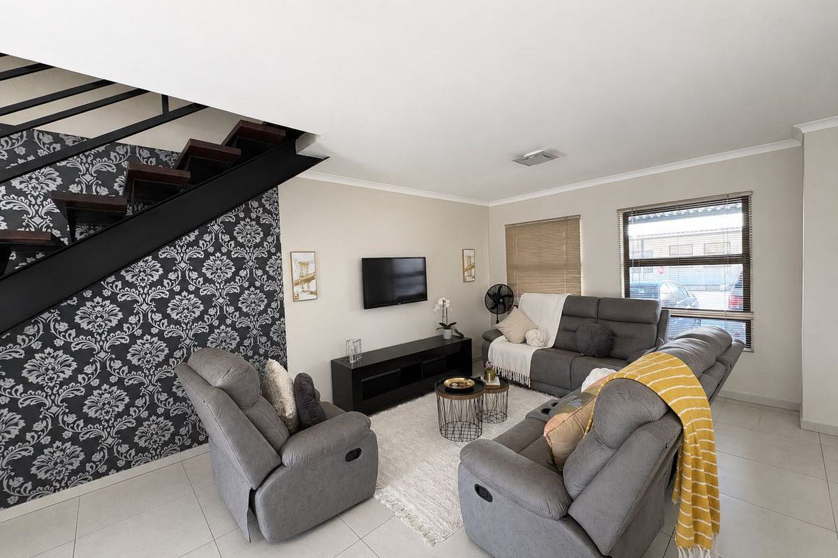A well-maintained living room featuring tiled flooring, a modern staircase with metal railings, and large windows with venetian blinds.