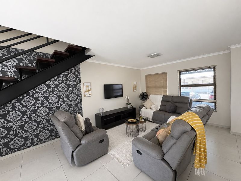 A well-maintained living room featuring tiled flooring, a modern staircase with metal railings, and large windows with venetian blinds.