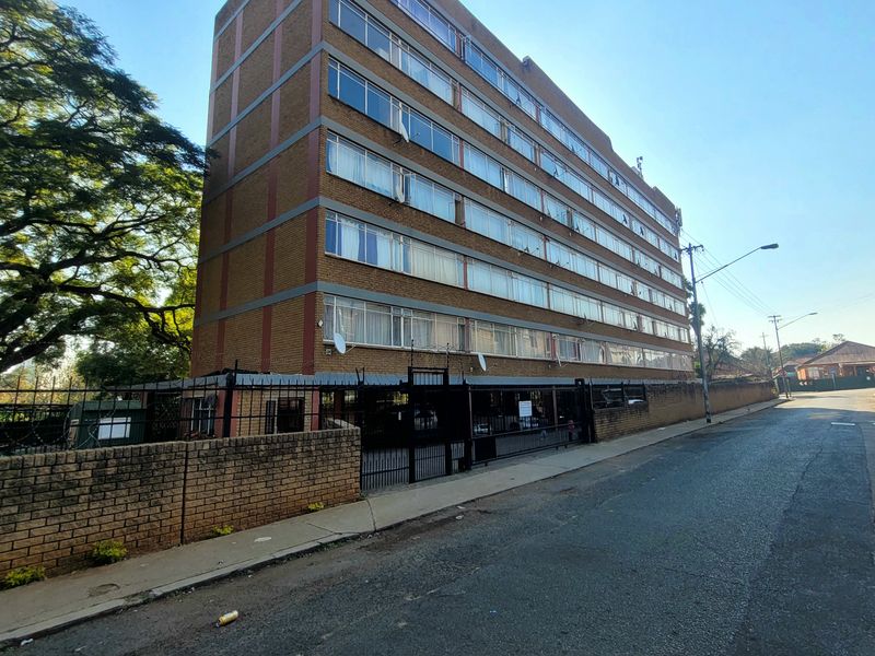 A multi-story brick apartment building featuring large windows, a secure perimeter wall with gate, and razor wire fencing along the street front.