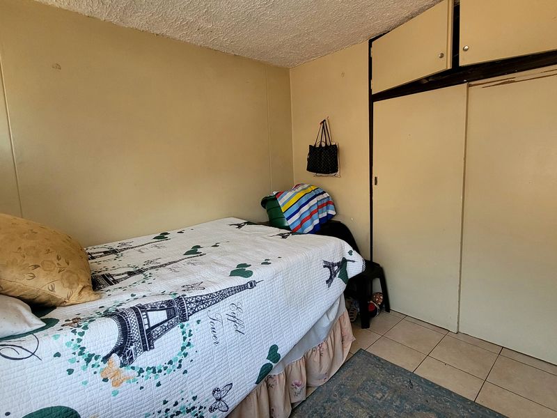 A bedroom featuring built-in cupboards, tiled flooring, and a textured ceiling, offering a functional space in need of cosmetic updates.