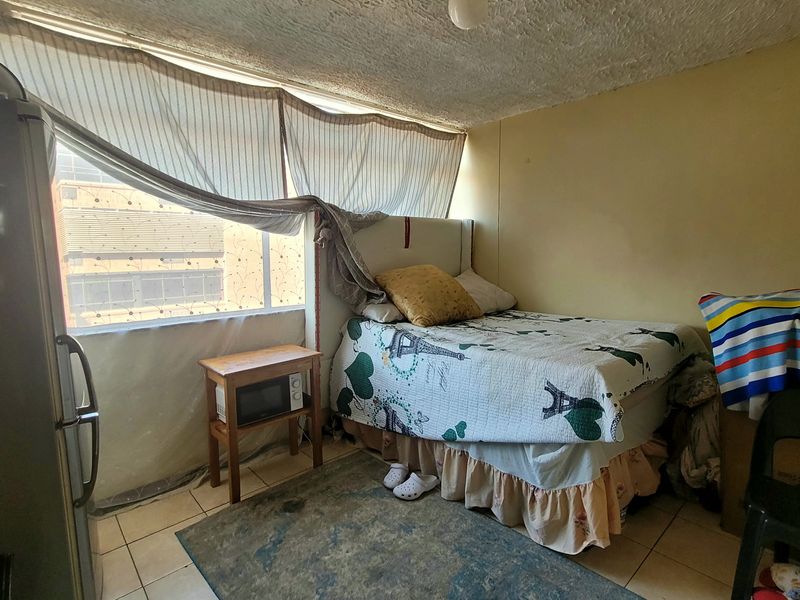 A compact bedroom featuring tiled flooring and a textured ceiling, currently in need of cosmetic updates and maintenance to improve its overall condition.