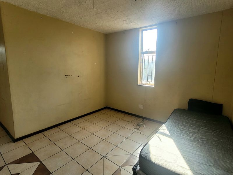 A vacant bedroom featuring tiled flooring and a window with security bars, requiring cosmetic updates to the walls and ceiling.